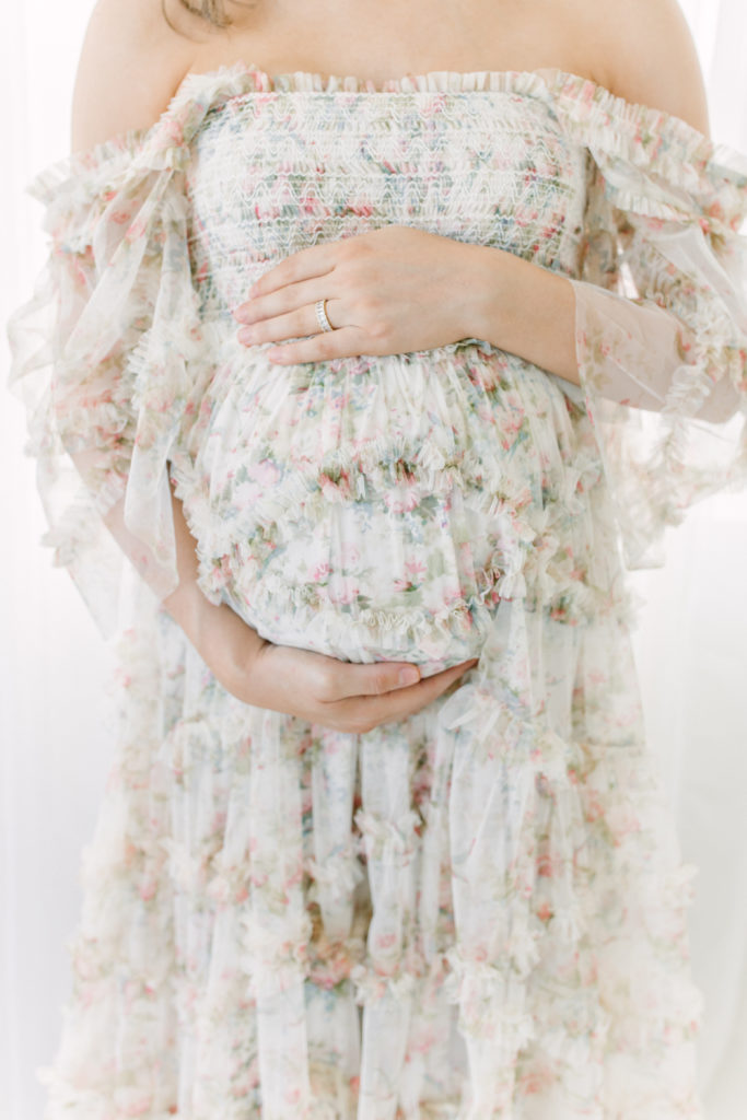 Expecting Mom cradles belly over beautiful floral dress in Atlanta Photography Studio. Spencer Livingston Photography is an Atlanta Newborn, Maternity, and Family
 Photographer.
