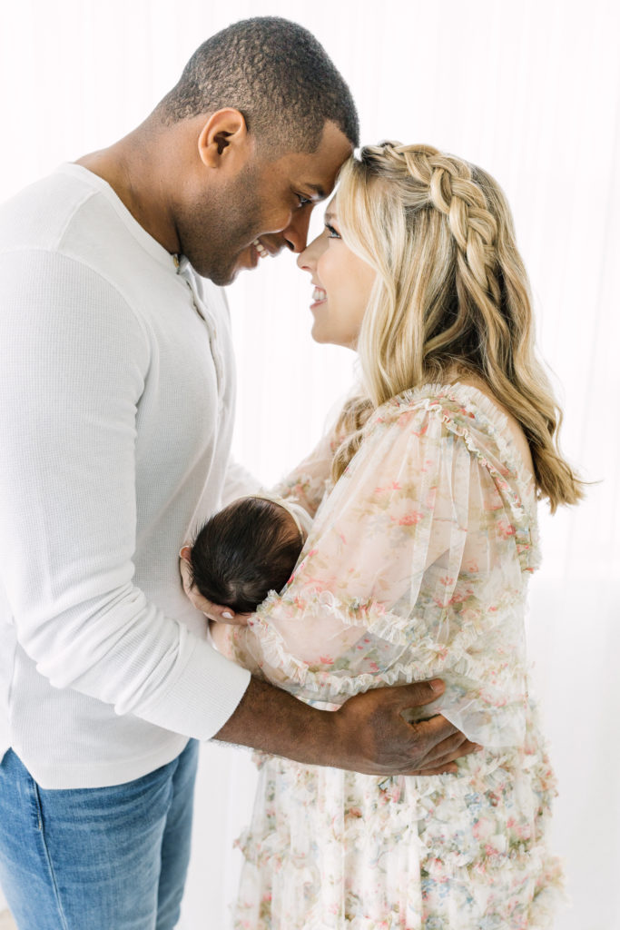 Mom and dad lean in close over their newborn daughter during her atlanta newborn photo session.