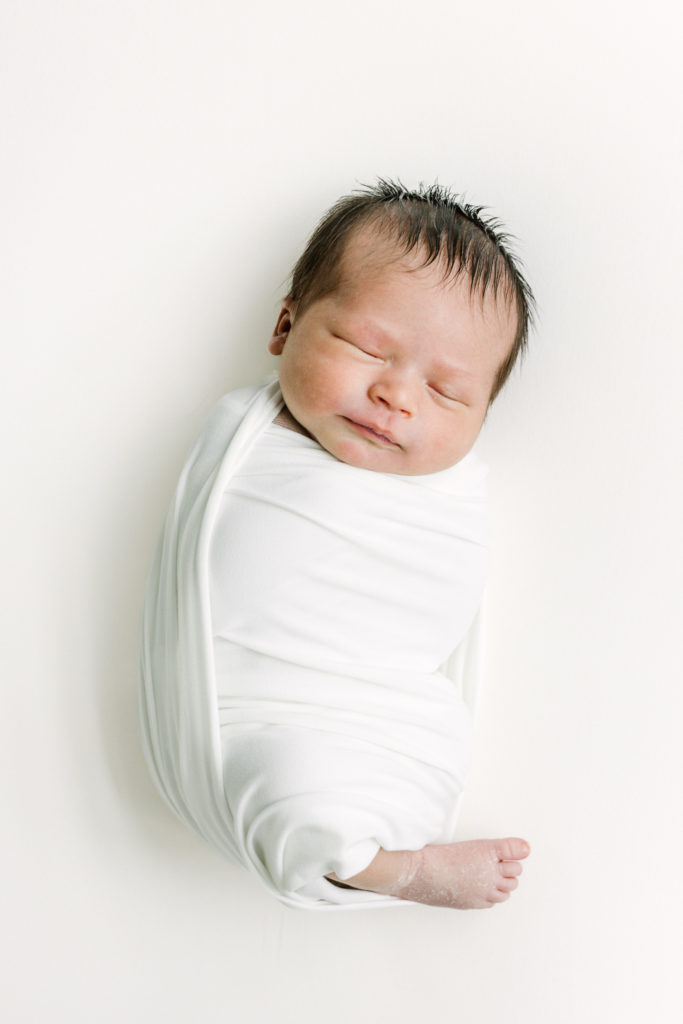 Newborn baby with dark hair lies on a photography bean bag.